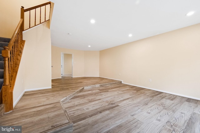 unfurnished living room featuring baseboards, stairs, light wood-style flooring, and recessed lighting