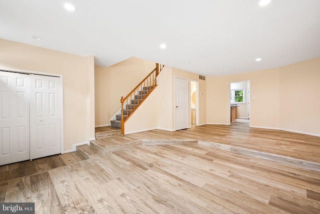 unfurnished living room featuring stairway, baseboards, and wood finished floors