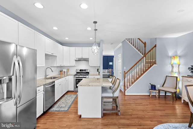 kitchen with appliances with stainless steel finishes, a sink, recessed lighting, under cabinet range hood, and a kitchen island