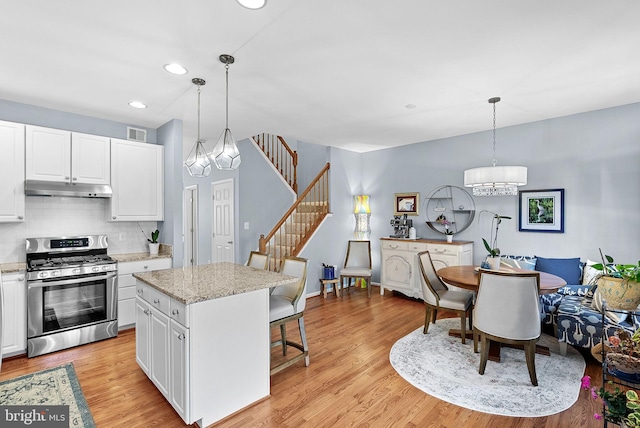 kitchen featuring stainless steel gas stove, a chandelier, under cabinet range hood, a kitchen breakfast bar, and recessed lighting