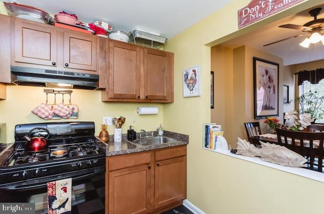kitchen with black range with gas cooktop, under cabinet range hood, ceiling fan, brown cabinets, and a sink
