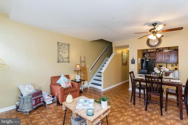 living area with stairs, a ceiling fan, and baseboards