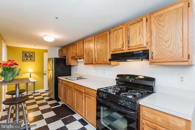 kitchen with black gas stove, under cabinet range hood, dark flooring, a sink, and freestanding refrigerator