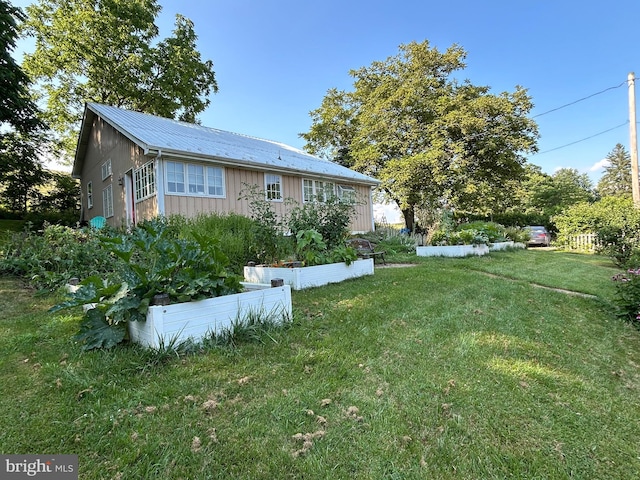 view of property exterior featuring metal roof, a vegetable garden, and a lawn