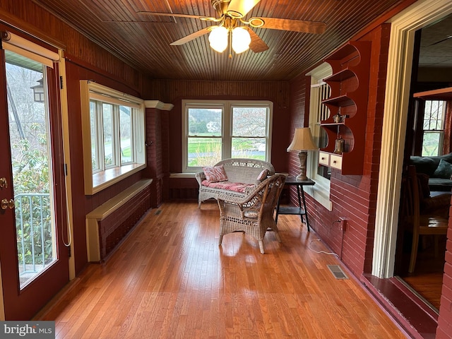 living area featuring a ceiling fan, light wood-type flooring, visible vents, wood walls, and wooden ceiling