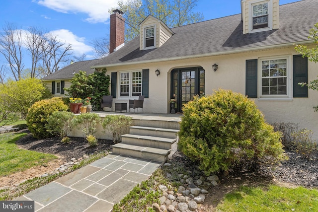 entrance to property with a chimney, stucco siding, and a shingled roof