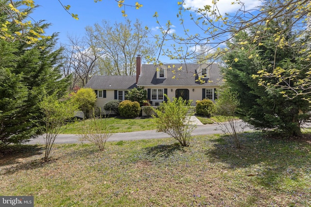 new england style home with a chimney, driveway, and a front yard