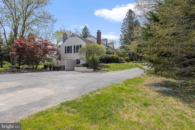 view of side of home featuring a chimney, a yard, and aphalt driveway
