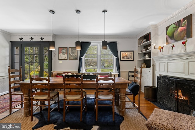dining area featuring wood finished floors, wainscoting, ornamental molding, built in features, and a lit fireplace