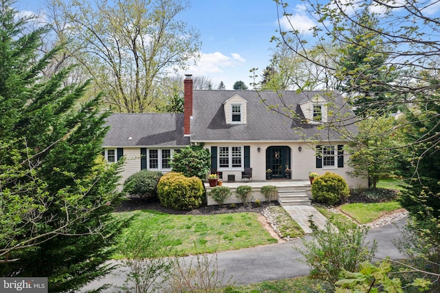 new england style home with covered porch, roof with shingles, stucco siding, and a chimney