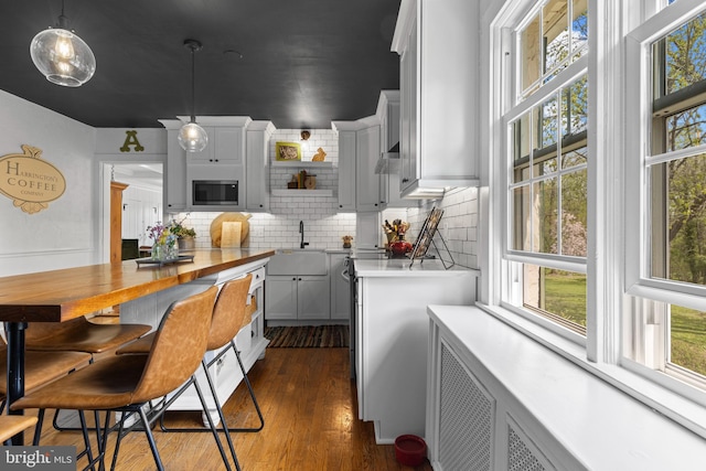 kitchen with open shelves, light countertops, stainless steel microwave, and a healthy amount of sunlight