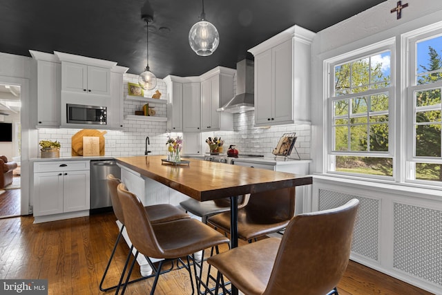 kitchen with stainless steel appliances, wooden counters, a healthy amount of sunlight, and wall chimney exhaust hood
