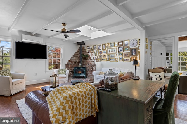 living area with a wall unit AC, plenty of natural light, ceiling fan, a wood stove, and beam ceiling