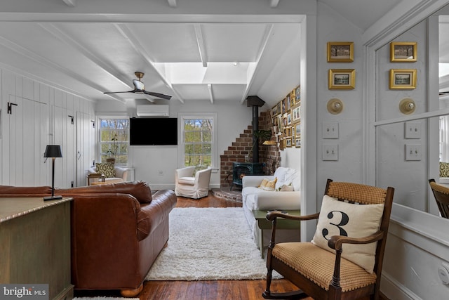 living area featuring wood finished floors, beamed ceiling, ceiling fan, a wood stove, and an AC wall unit