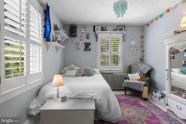 bedroom with baseboards, radiator heating unit, and a textured ceiling