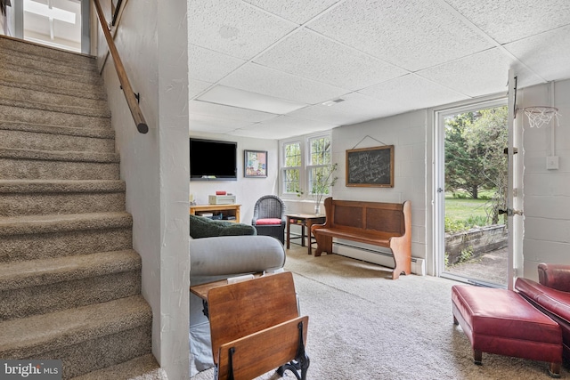carpeted living room featuring a drop ceiling, stairway, baseboard heating, and concrete block wall