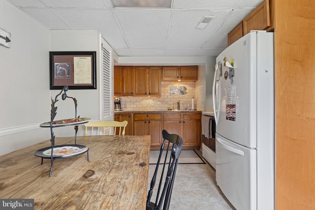 kitchen with freestanding refrigerator, backsplash, and a drop ceiling
