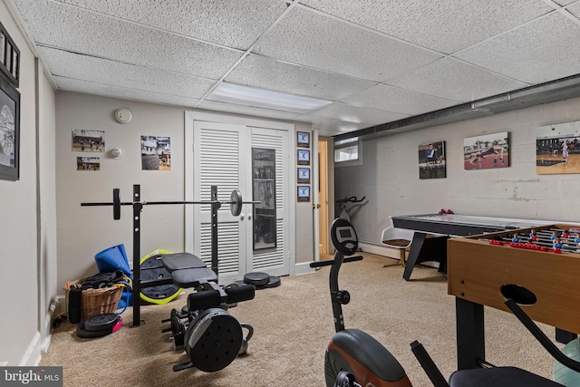 exercise room with carpet, a drop ceiling, concrete block wall, baseboards, and a baseboard heating unit