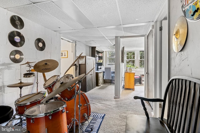 basement featuring a paneled ceiling, carpet, and concrete block wall