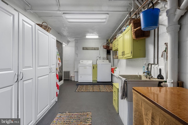 laundry area featuring washing machine and clothes dryer, radiator, concrete block wall, and cabinet space
