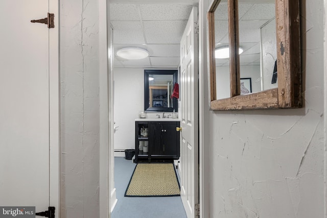 hall with a drop ceiling, carpet, and a textured wall