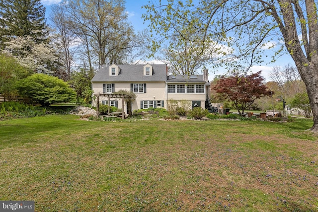 rear view of property with stairway, a chimney, and a lawn