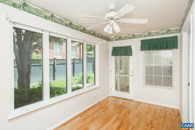 unfurnished sunroom with a deck, baseboards, and wood finished floors