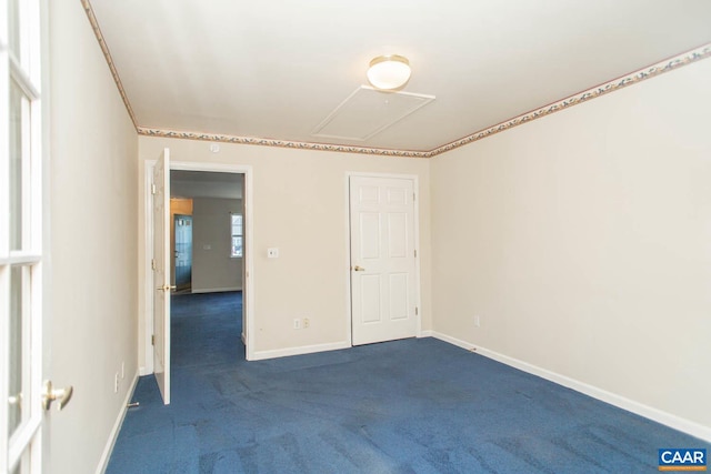 empty room featuring baseboards, dark colored carpet, and attic access