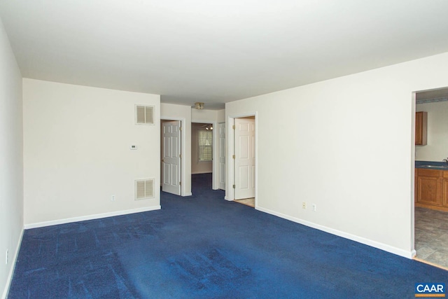 spare room featuring baseboards, visible vents, and dark carpet
