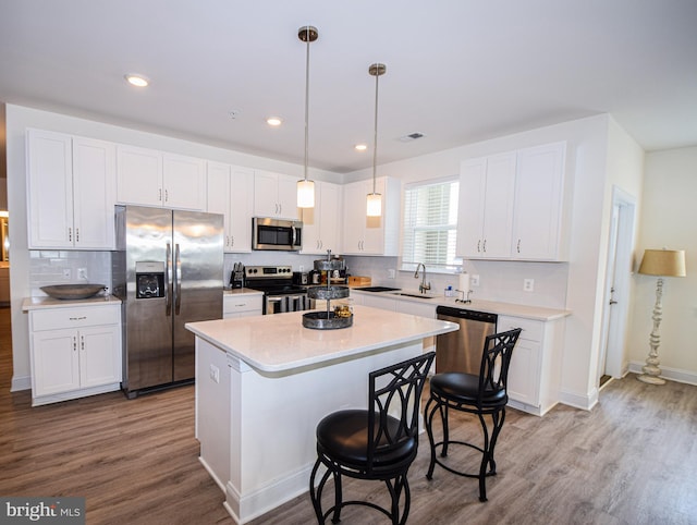 kitchen with stainless steel appliances, a sink, wood finished floors, white cabinets, and recessed lighting