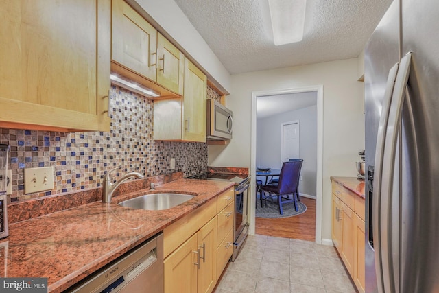 kitchen featuring stainless steel appliances, a sink, decorative backsplash, a textured ceiling, and stone counters