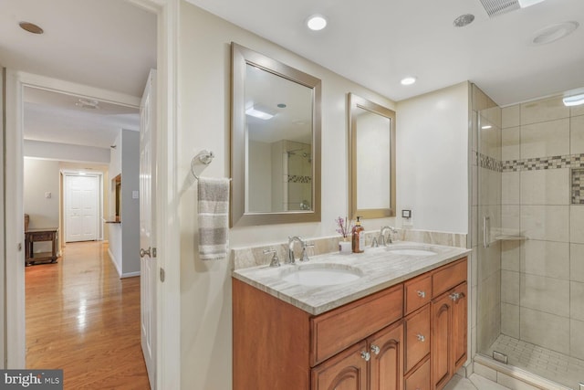 bathroom featuring wood finished floors, a shower stall, double vanity, and recessed lighting