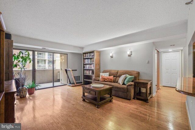 living room featuring light wood-type flooring, a textured ceiling, and baseboards
