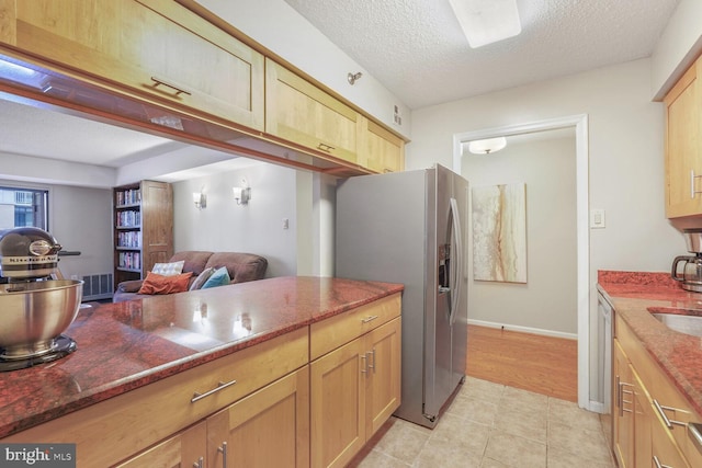 kitchen with stainless steel appliances, dark stone countertops, a textured ceiling, open floor plan, and light brown cabinetry
