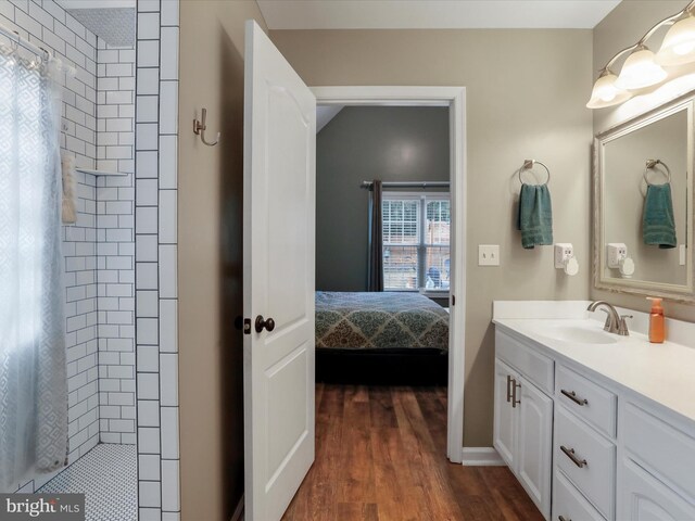 ensuite bathroom featuring tiled shower, vanity, and wood finished floors