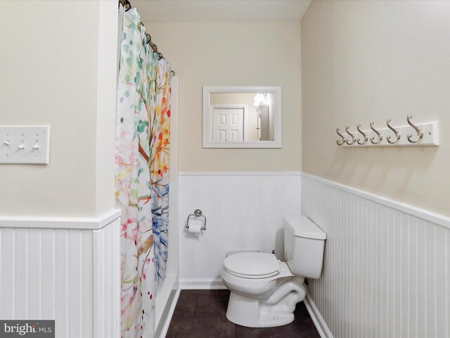 full bathroom with a wainscoted wall, toilet, and tile patterned flooring