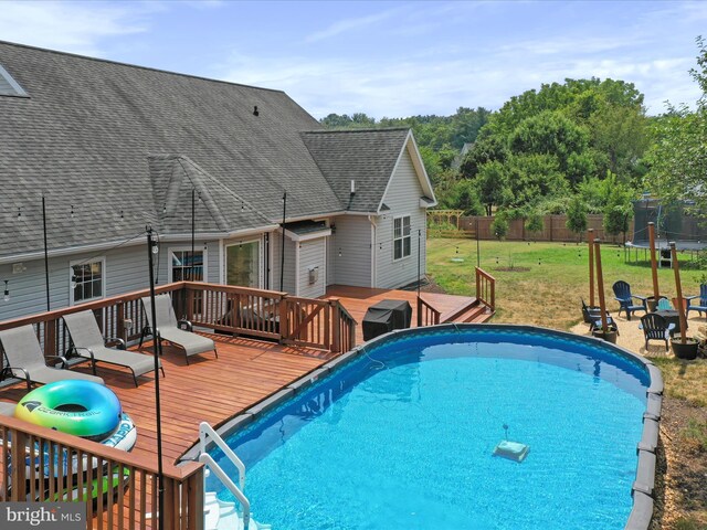 view of pool featuring a trampoline, a wooden deck, and a fire pit