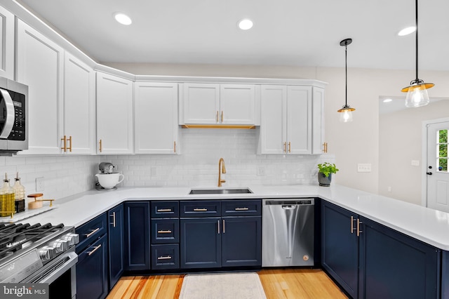 kitchen with stainless steel appliances, a sink, blue cabinetry, light countertops, and white cabinetry