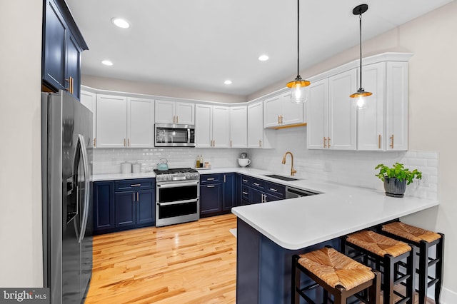 kitchen with appliances with stainless steel finishes, blue cabinetry, a sink, a peninsula, and light countertops