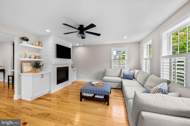 living room with light wood finished floors, a ceiling fan, recessed lighting, a glass covered fireplace, and baseboards