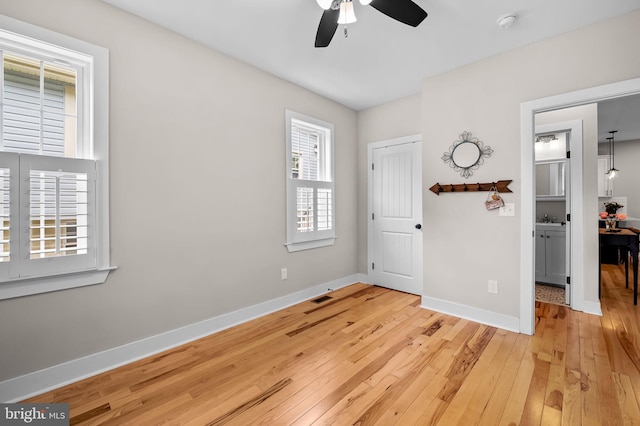 empty room featuring a ceiling fan, light wood-type flooring, and baseboards