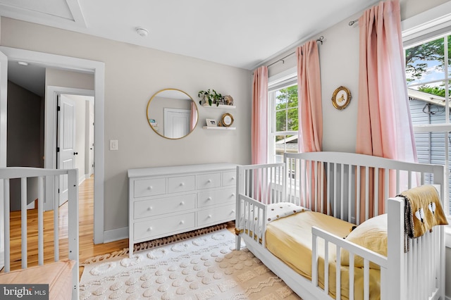 bedroom with light wood-type flooring, baseboards, and a nursery area