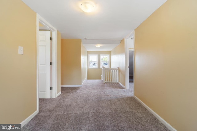 hall featuring carpet floors, baseboards, and an upstairs landing