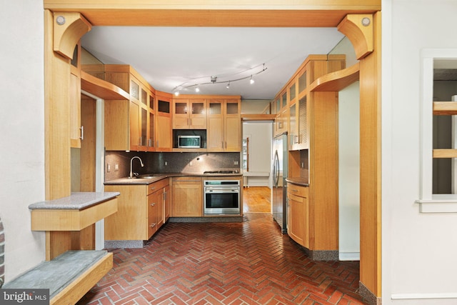 kitchen with stainless steel appliances, a sink, tasteful backsplash, glass insert cabinets, and brick floors