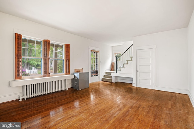 unfurnished room featuring radiator heating unit, wood finished floors, stairs, and baseboards