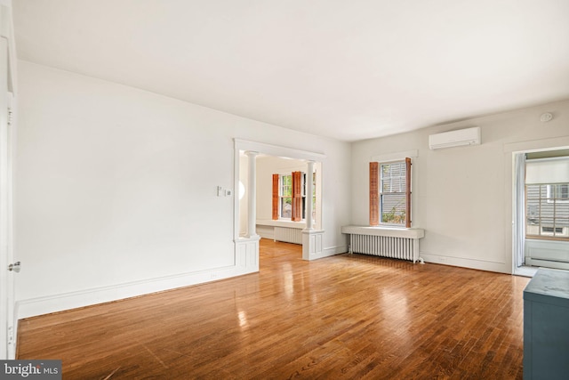 unfurnished room featuring radiator heating unit, a wall mounted air conditioner, wood finished floors, and healthy amount of natural light
