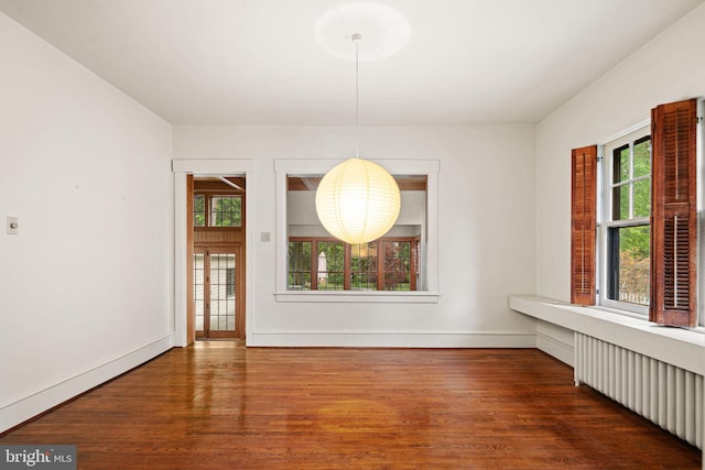 unfurnished dining area with wood finished floors, healthy amount of natural light, baseboards, and radiator