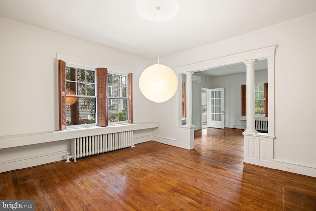 unfurnished dining area featuring radiator heating unit, decorative columns, wood finished floors, and an AC wall unit