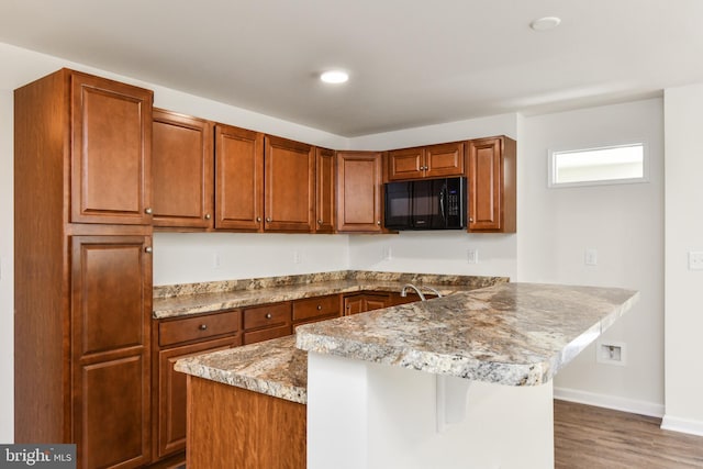 kitchen featuring black microwave, a peninsula, a kitchen breakfast bar, wood finished floors, and brown cabinets