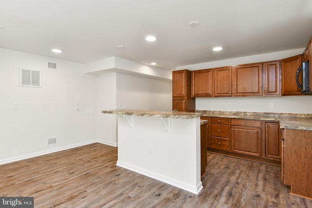 kitchen featuring brown cabinets, a breakfast bar area, wood finished floors, recessed lighting, and baseboards